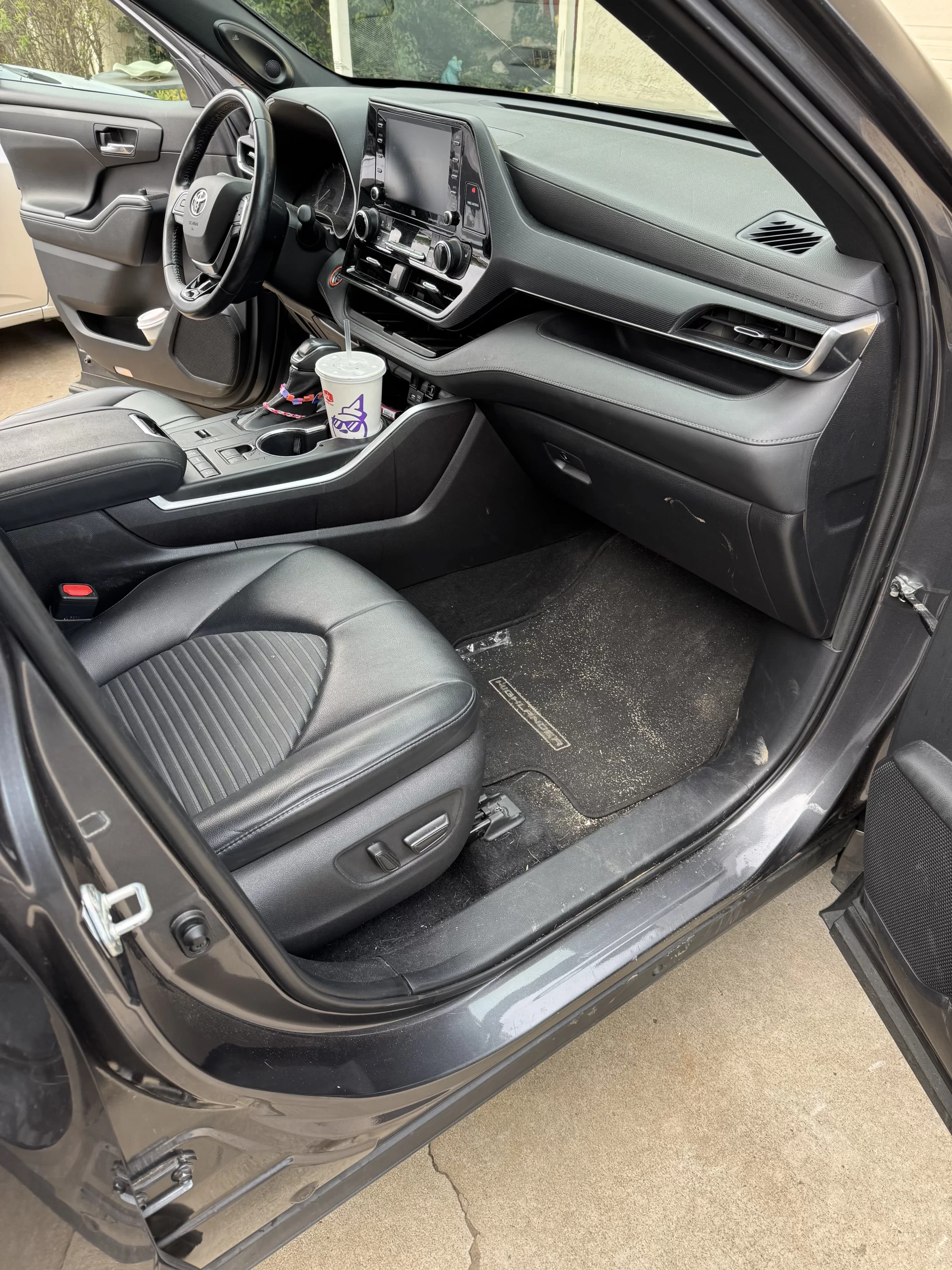 Front passenger seat and interior of a modern car with black leather seats, a touchscreen dashboard, a cup in the center console, and some dirt visible on the floor mat. - DNC Auto Detailing in Ramona, California