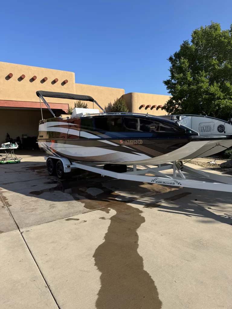 A sleek black and white speedboat on a trailer is parked on a driveway in front of a southwestern-style house, with trees and another boat visible nearby. - DNC Auto Detailing in Ramona, California